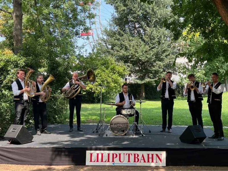 Blasmusik-Band mit Schlagzeug auf Open-Air-Bühne im Prater, Tontechnik im Einsatz.