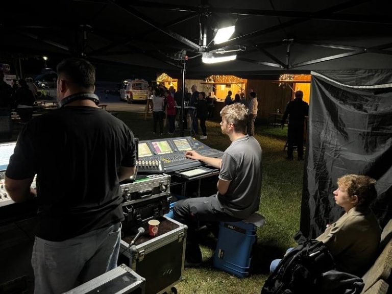 Eventpower Techniker bei Nacht am Lichtpult, beleuchtet von Scheinwerfer, während er die Bühnenbeleuchtung steuert.